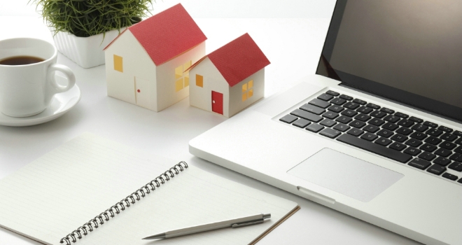 A laptop next to some house paperweights and a notepad and pen